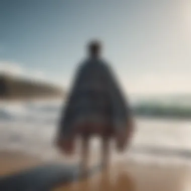 A surfer putting on a changing robe poncho after a surf session, with ocean waves in the background.